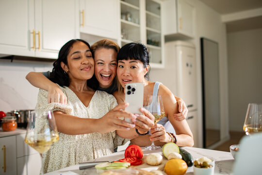 Three friends taking a selfie while cooking with wine in a modern kitchen