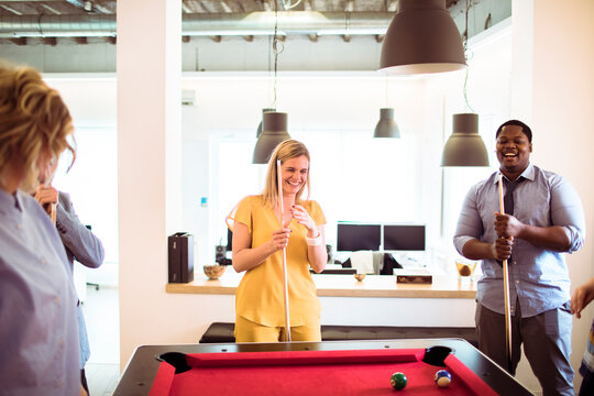 Happy coworkers playing pool in modern office breakroom