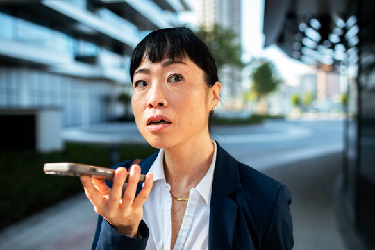 Businesswoman using voice assistant on smartphone in city street