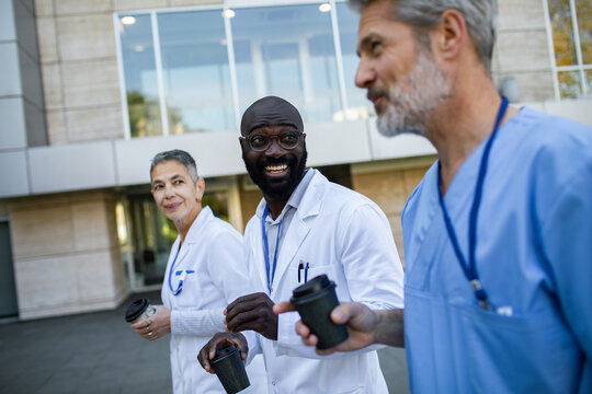 Smiling doctors walking with coffee outside hospital