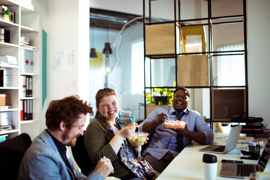 Happy coworkers eating lunch together in modern office