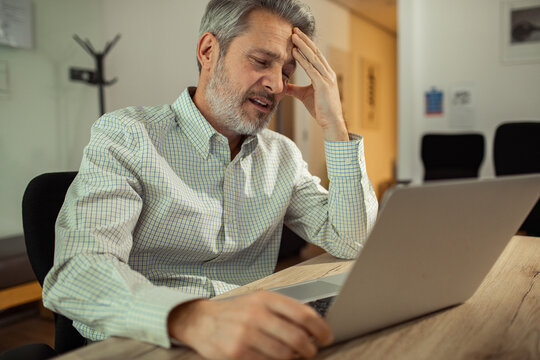 Stressed middle-aged man working on laptop in office