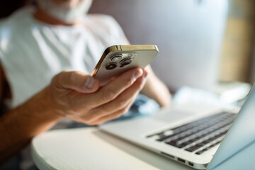 Fototapeta premium Senior man using smartphone with laptop at home