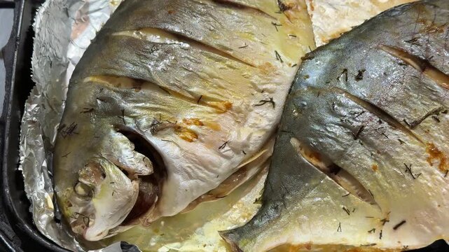 Oven roasted pompano on black platter two golden sea fish scored and roasted in foil top view showing crispy skin browned edges