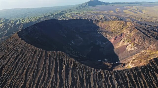 Aerial view showing the majestic Ambrym Island caldera featuring the craters of Benbow and Marum volcanos, a raw volcanic landscape with barren ground and distant green vegetation. Drone panorama