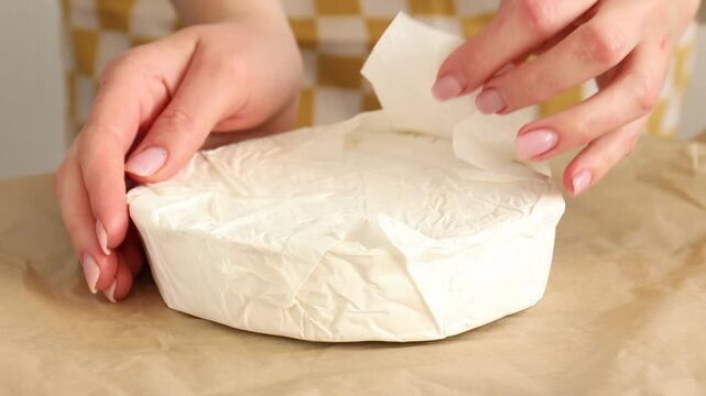 Woman showing delicious brie cheese at table, closeup