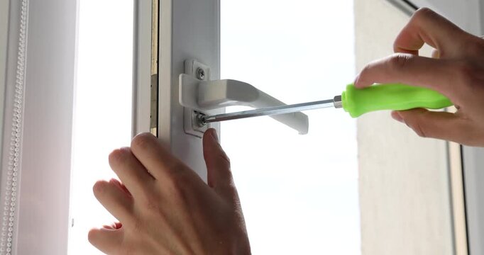 Worker with screwdriver installing window handle indoors, closeup