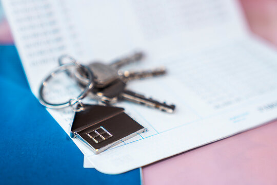 House keys with a metal house shaped keychain lying on an opened bank passbook. Concept of real estate investment, buying a new home, mortgage loan, and property financial savings.