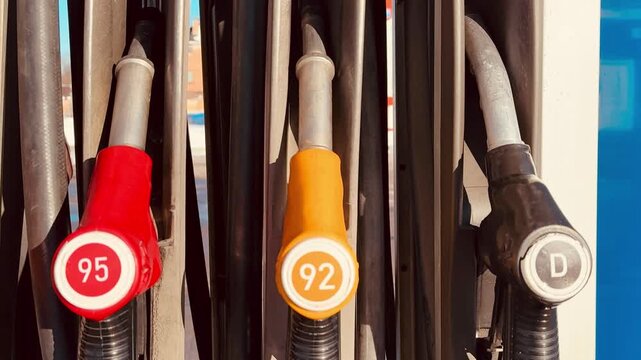 Closeup gas pump nozzles red yellow, octane labels and diesel marker, metal handles and rubber hoses, sunlight highlights textured