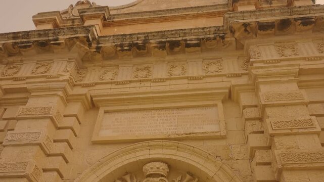 Cinematic approach and tilt-up reveal of Mdina Main Gate with historic limestone fortress walls in Malta