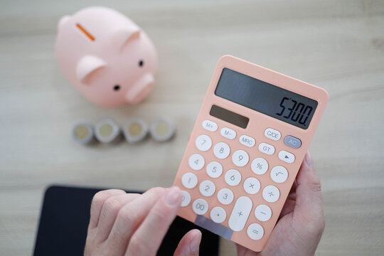 
Man sits at desk, thoughtful, pen in hand. Piggy bank and coins rest nearby, symbolizing savings. He sketches ideas on notebook, surrounded by charts. Office shelves hold colorful folders