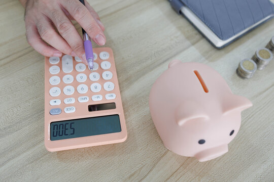 
Man sits at desk, thoughtful, pen in hand. Piggy bank and coins rest nearby, symbolizing savings. He sketches ideas on notebook, surrounded by charts. Office shelves hold colorful folders