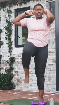 Vertical video: Starting woman pink tee leggings alternating high-knees on patio mat for cardio