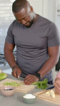 Vertical video: Cutting man in gray tee using chef knife, slicing celery in kitchen starting prep