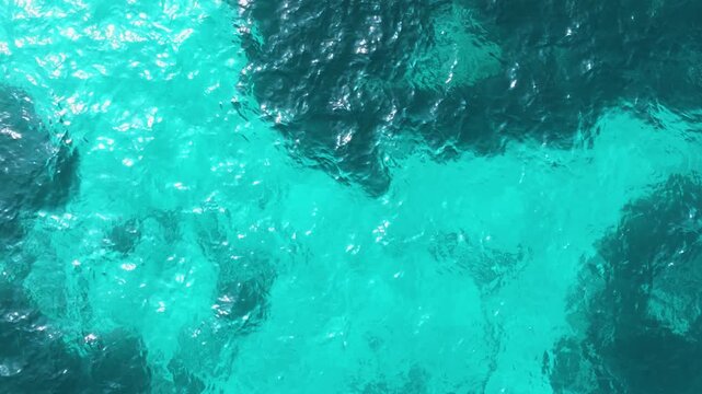 Cinematic low drone flight over crystal clear turquoise Mediterranean water along limestone coast Malta drone moves smoothly forward just above the water surface, revealing detailed underwater texture