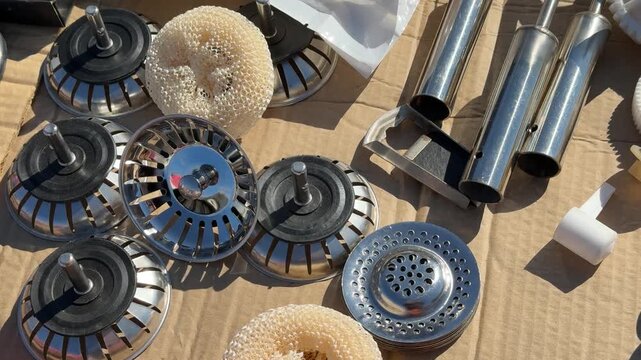 Chrome sink strainers and drain parts laid on cardboard with spare plugs, metal tubes, foam gaskets and cleaning sponge, bright
