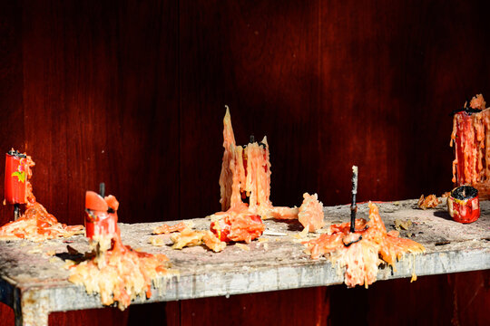Candle wax drips and pools on an old altar, showing traces of devotional offerings against a dark wooden background.