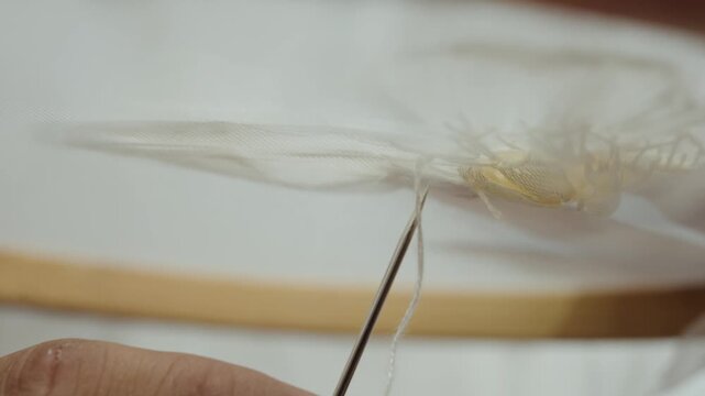 Macro shot of needle and thread stitching handmade flower applique for luxury wedding dress production
