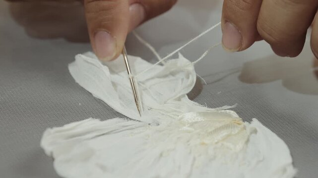 Fashion artisan stitching handmade floral applique with needle and thread during bridal couture process