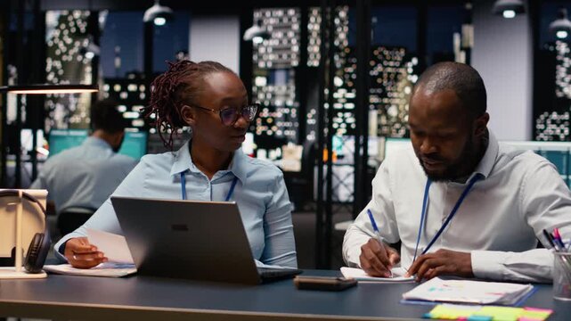 Two staff members reading emails and solving tasks together on laptop at desk, office workers analyzing data on notebook. Accounting work and interpreting statistical information.