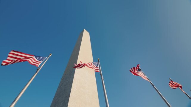 Washington monument American flags waving in wind against clear blue sky low angle view.