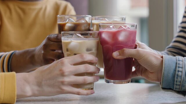 Friends clinking glasses with iced coffee and cold drink during gathering. Group of people making toast with refreshing beverages at cafe. Celebration of friendship and social connection concept