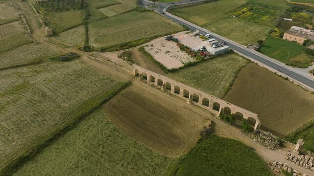 Cinematic drone orbit around historic Gozo Aqueduct near Victoria Malta. remaining limestone arches of  19th-century structure stretch across the rural landscape, creating striking geometric pattern