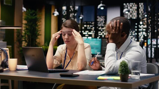 Burnout and frustration, two colleagues struggling to stay awake and solve tasks, worried of missing deadline late at night. Diverse people with low energy and exhaustion overwhelmed by work.