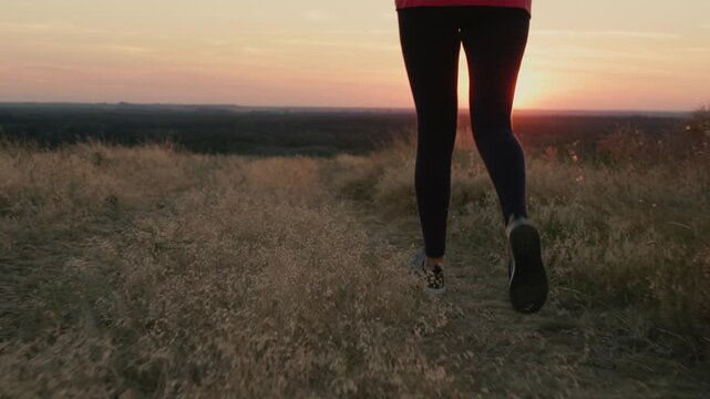 Woman running on grassy hill during golden sunset creating dynamic cinematic outdoor exercise footage.