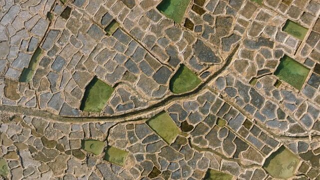 Top-down drone tracking movement over salt pans on Gozo Malta with lateral parallel motion. camera remains fixed vertically downward, revealing a continuous geometric grid of rectangular salt basins 