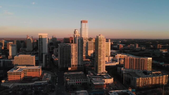 Aerial drone footage captures bustling Austin skyline at sunset with modern skyscrapers and city lights illuminating the dusk.