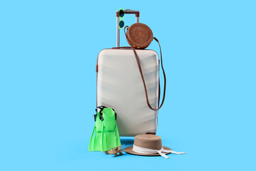 White suitcase with wicker bag, stylish hat, wooden airplane and flippers on blue background © Pixel-Shot