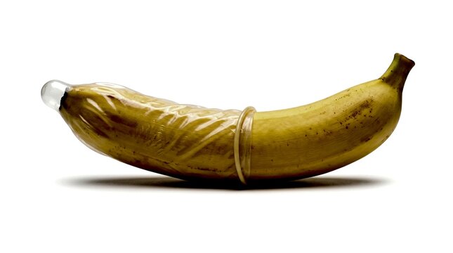 Banana with a rolled latex condom isolated on a white background for safe sex education, contraception awareness, reproductive health, and medical advertising.