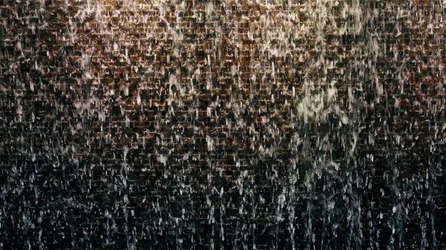 Dubai water wall feature with cascading droplets flowing down illuminated textured surface. Golden light reflects through streams creating mesmerizing patterns against dark backdrop.