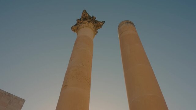 Two remaining stone columns of Royal Opera House ruins in Valletta, Malta against blue sky, low angle upward cinematic view of WWII historic architectural remains