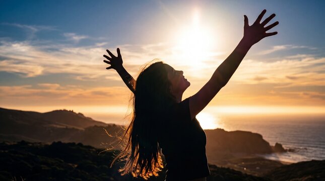 A young girl stands back-lit with arms open wide to a coastal golden sunset, her hair catching the warm light. The image evokes absolute freedom, joy, and hope.