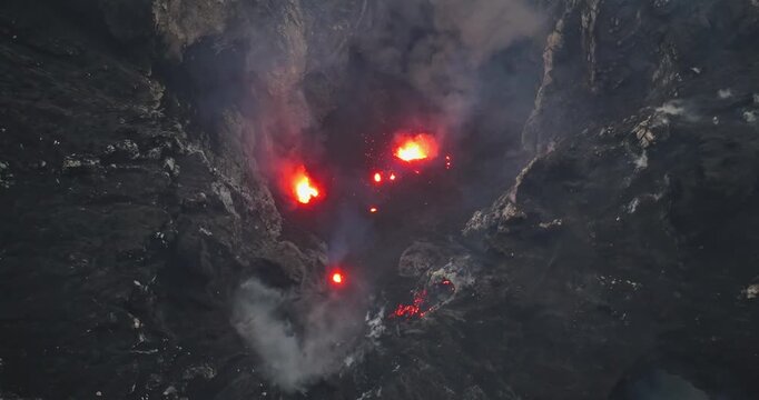 Mt. Yasur volcano powerfully erupting at Port Resolution, Tanna Island, showing molten lava flowing and active smoke rising from the dark, rugged crater rim. Dramatic landscape. Aerial view drone shot