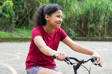 Obraz premium Smiling Latina girl riding bicycle outdoors during active childhood moment in neighborhood park