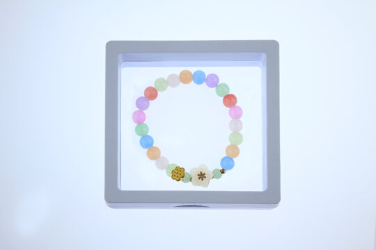 Colorful beads with decorative flower charm presented in modern plastic display case.  Cute pastel beaded bracelet with decorative flower displayed inside transparent frame isolated white background.