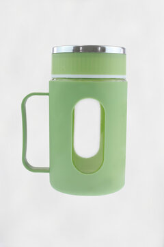 Pastel green mug with handle and lid. Transparent sleeve adds grip and style. Modern design for hot or cold drinks. Ideal for offices, cafes, or home use. Simple background highlights product details.