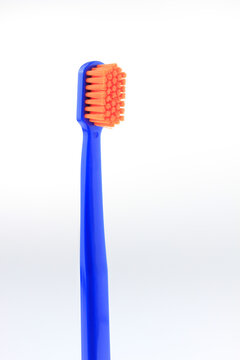 Blue toothbrush with orange bristles stands upright, isolated white background  with copy space. Minimalist style emphasizes product design. Ideal for dental care, hygiene campaigns, dental education