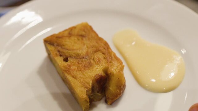 Pouring Creamy Custard Sauce onto a White Plate with Bread Pudding