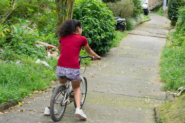 Fototapeta premium Young Latina girl riding bicycle downhill on asphalt street in a low income neighborhood outdoors