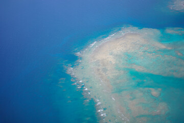 Obraz premium Aerial view of beautiful coral reef and turquoise ocean from airplane window