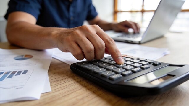 Close up of businessman hands using calculator for accounting and financial analysis, office desk with charts, laptop in background, tax calculation, budget planning, corporate