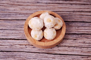 Fototapeta premium Kue Salju Soft, powdered treats rest in a wooden bowl. Warm wood grain adds rustic charm. Minimalist background emphasizes sweet delicacy. Gentle lighting enhances inviting texture. Ideal for food 