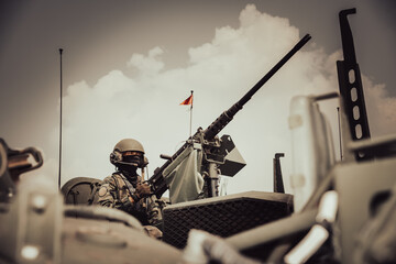 Close-up of a military soldier wearing tactical gear and a helmet operating a heavy machine gun mounted on a turret during an army exercise. © Sirirat Makprasert