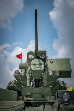 Low angle view of a modern military remote weapon station (RWS) equipped with a heavy machine gun, optical sensors, and smoke grenade launchers under a blue sky.