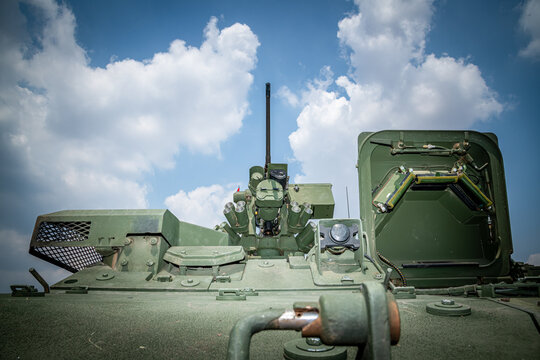 Low angle view of a modern military remote weapon station (RWS) equipped with a heavy machine gun, optical sensors, and smoke grenade launchers under a blue sky.