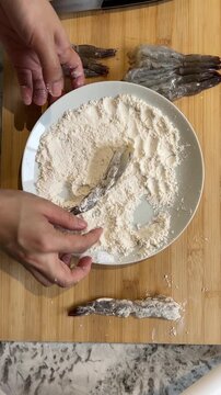 Enthusiastic asian female influencer creating food vlog using smartphone recording passionate home cooks coating raw shrimp and fresh fish with white flour on wooden board for delicious meal